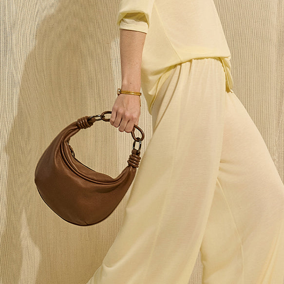 Banner de vitrine modelo usando roupa amarela e usando bolsa de couro mini hobo marrom da marca Soleah