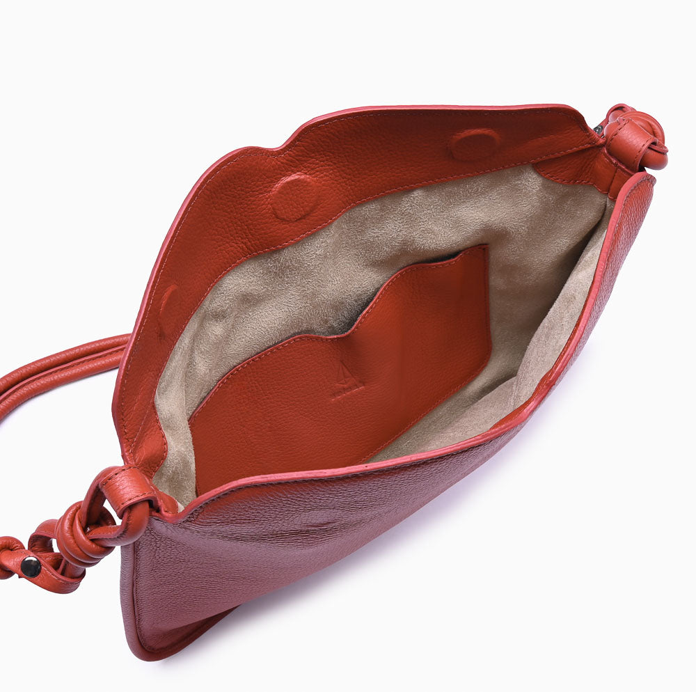 Flap Loop Soleah em couro vermelha: bolsa com aba frontal, formato compacto e alça longa para uso no ombro ou transversal; bolsa aberta em detalhe, mostrando o compartimento interno, o forro e o acabamento das bordas.